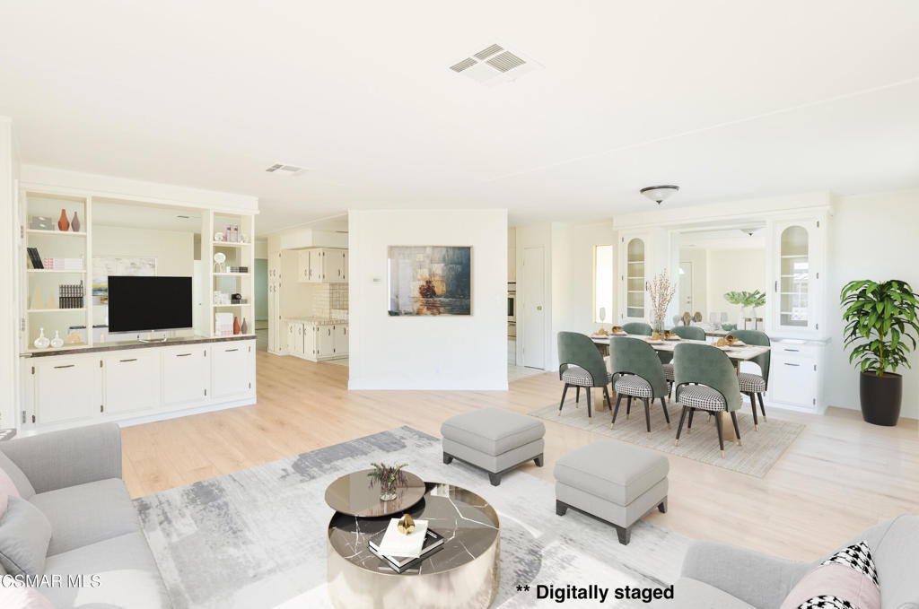 Open-plan living and dining room with white built-ins, light wood floors, and digitally staged furnishings.
