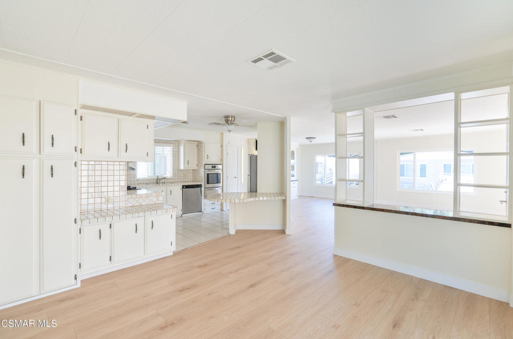 Empty kitchen and dining area with white cabinetry, tiled backsplash, and light wood flooring.