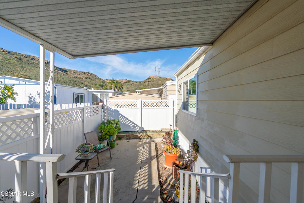 Covered patio with white fencing, potted plants, and hills beyond.