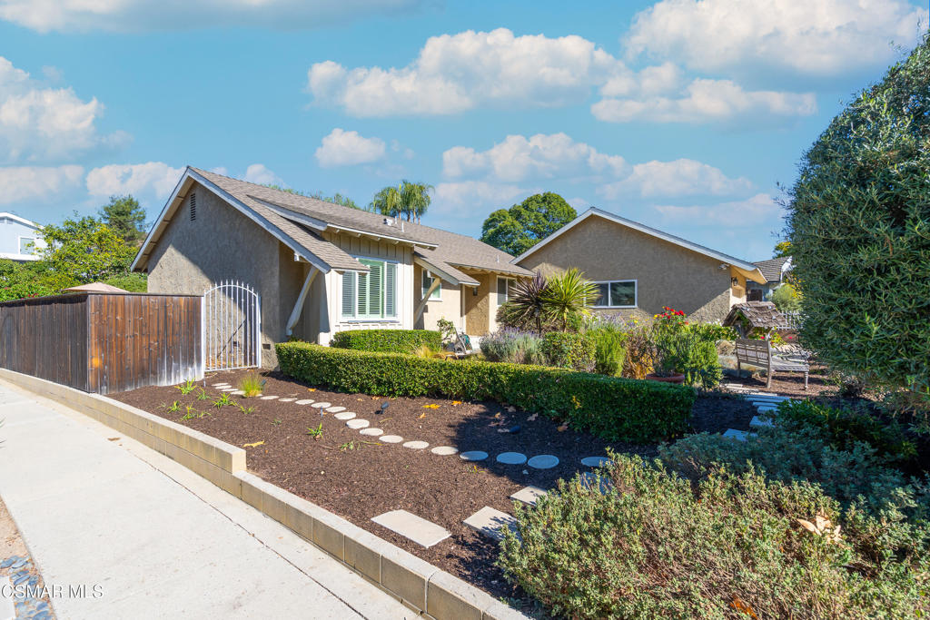 Single-story gray stucco home with a landscaped front yard, stepping stones, and a white metal gate.