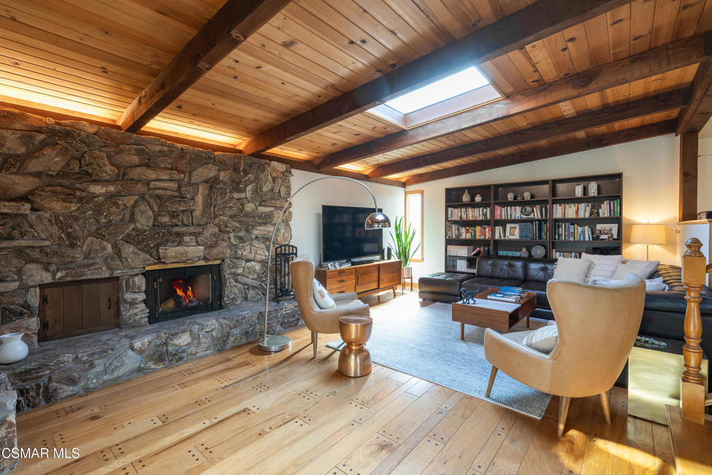 Living room with stone fireplace, exposed timber beams, skylight, and built-in bookshelves.