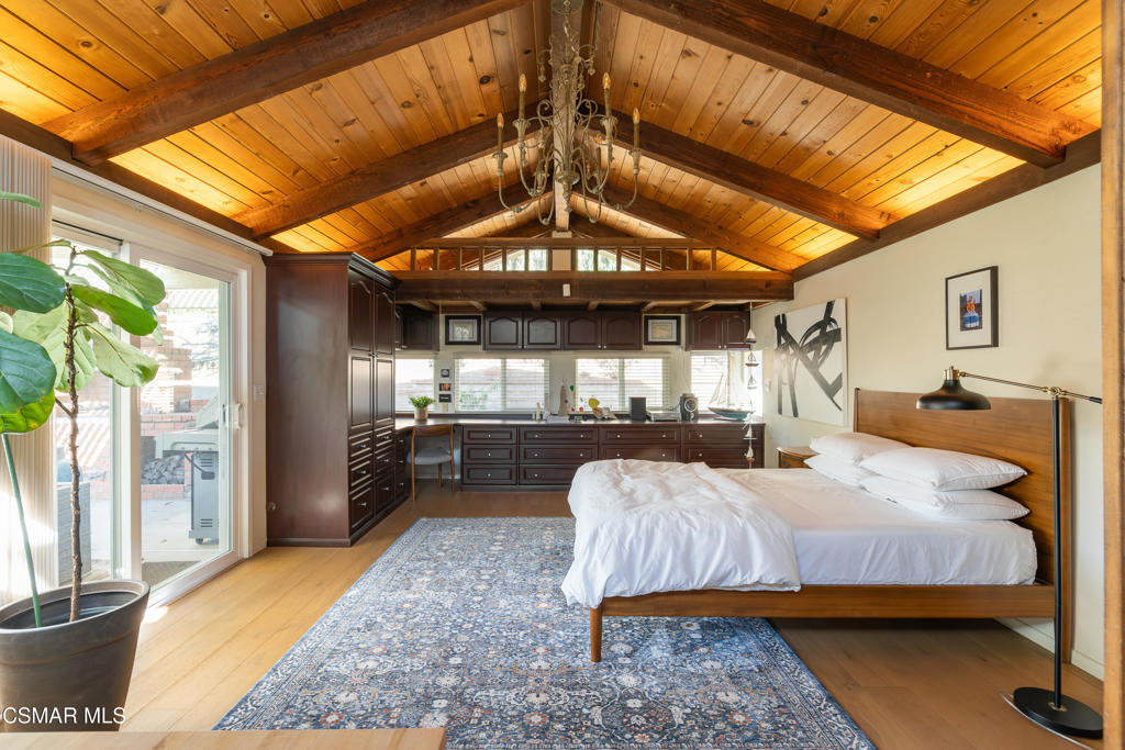 Bedroom with a vaulted wood ceiling, exposed beams, chandelier, and king bed.