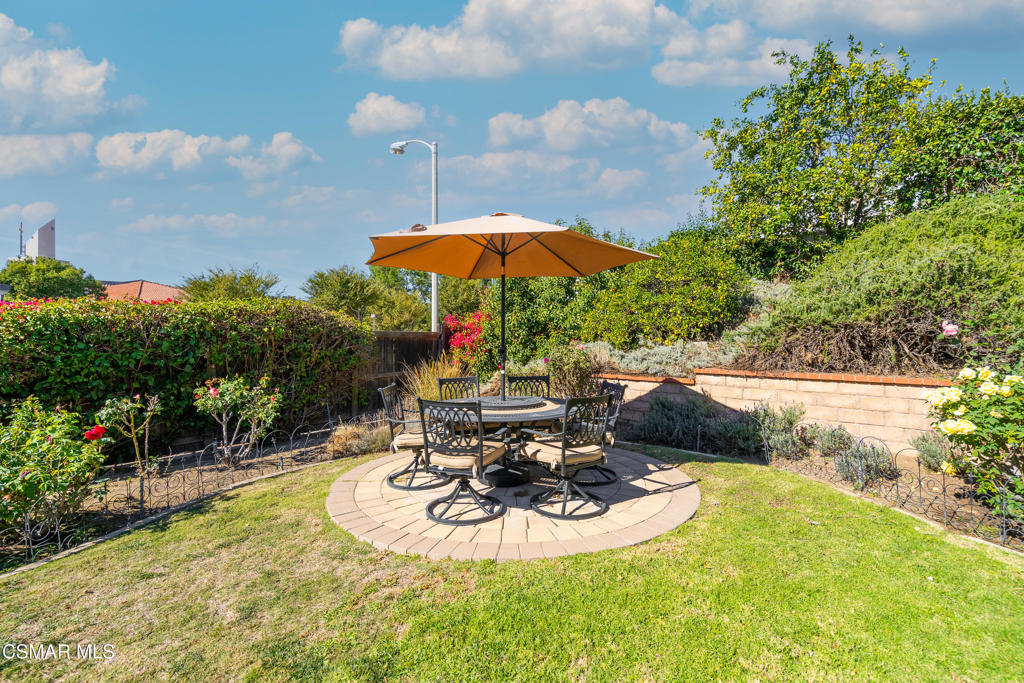 Backyard patio with circular dining area, orange umbrella, lawn, and flowering garden beds.