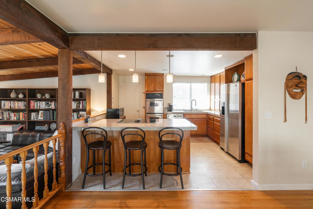 Kitchen with a wood island, three bar stools, stainless steel appliances, and exposed ceiling beams.