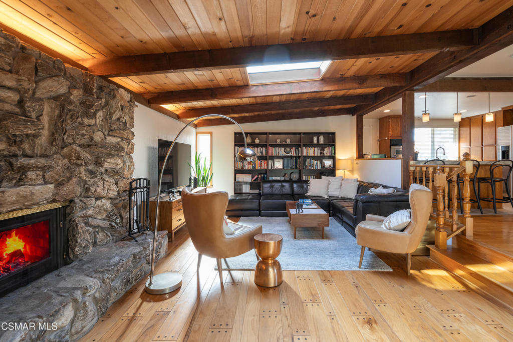 Living room with a stone fireplace, exposed wood beams, and a black sectional sofa.