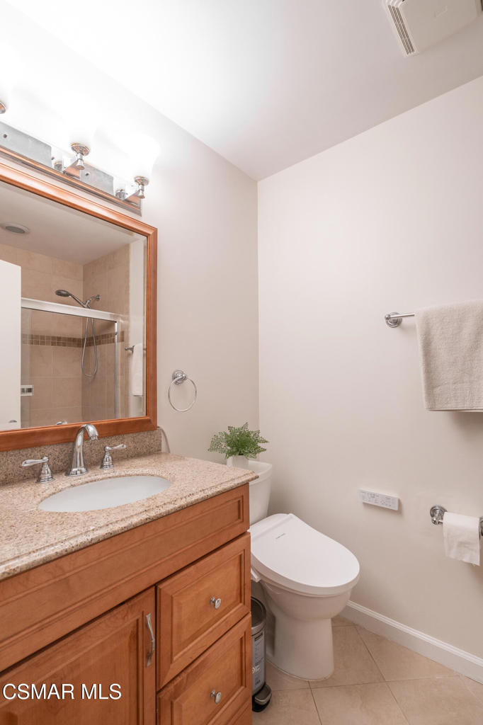 Bathroom with a wood vanity and granite countertop beside a toilet and tiled shower.