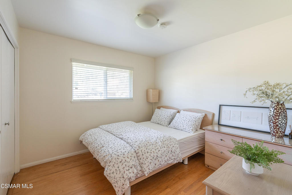 Bedroom with a floral-covered bed, window blinds, wood flooring, and a dresser.