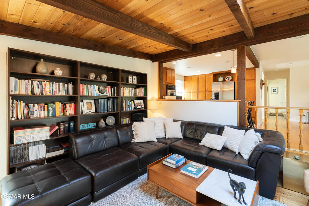 Living room with a black leather sectional, built-in bookshelves, and a wood-plank ceiling with exposed beams.