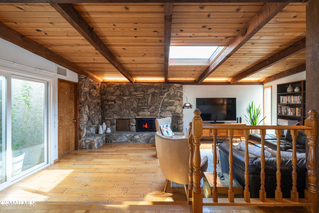 Living room with a stone fireplace, vaulted wood ceiling, skylight, and sliding glass doors.