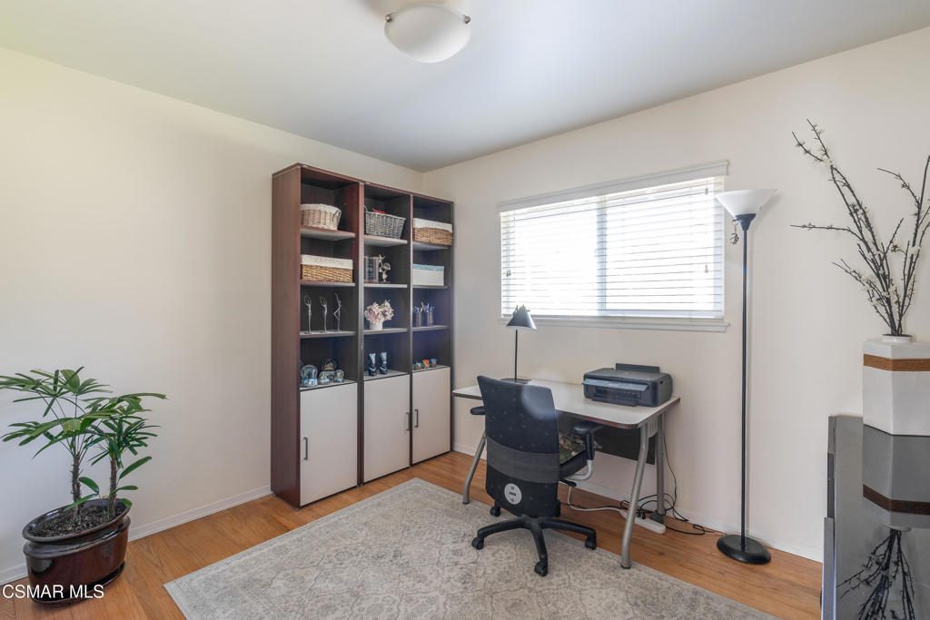 Home office with tall shelving, a desk and printer beside a window with blinds.