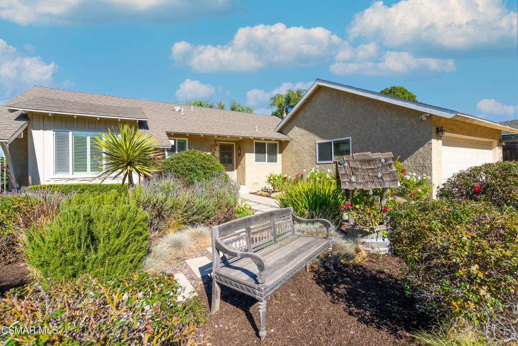 Single-story home with a two-car garage, landscaped garden, and wooden bench in front.