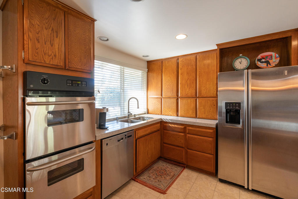 Kitchen with warm wood cabinetry, granite counters, stainless steel appliances, and a sink beneath a window.