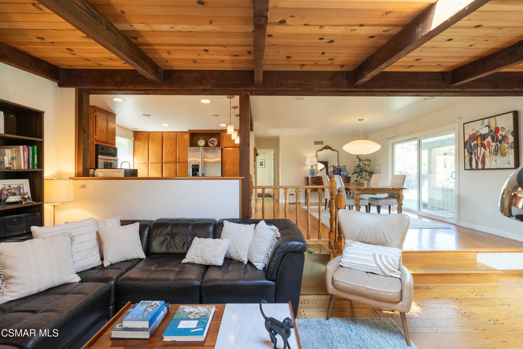 Living room with exposed wood beams, a dark leather sectional, and an adjoining kitchen and dining area.