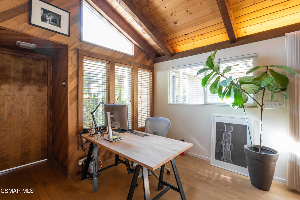 Home office with a vaulted wood ceiling, desk, and large potted plant.