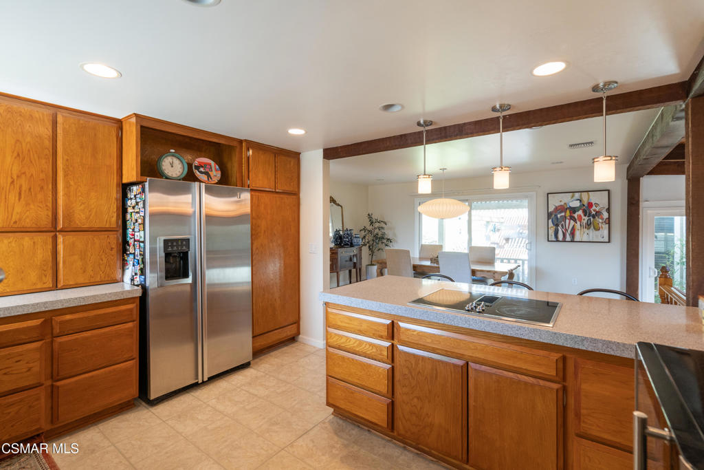 Kitchen with warm wood cabinets, stainless steel refrigerator, and a large island with a cooktop.