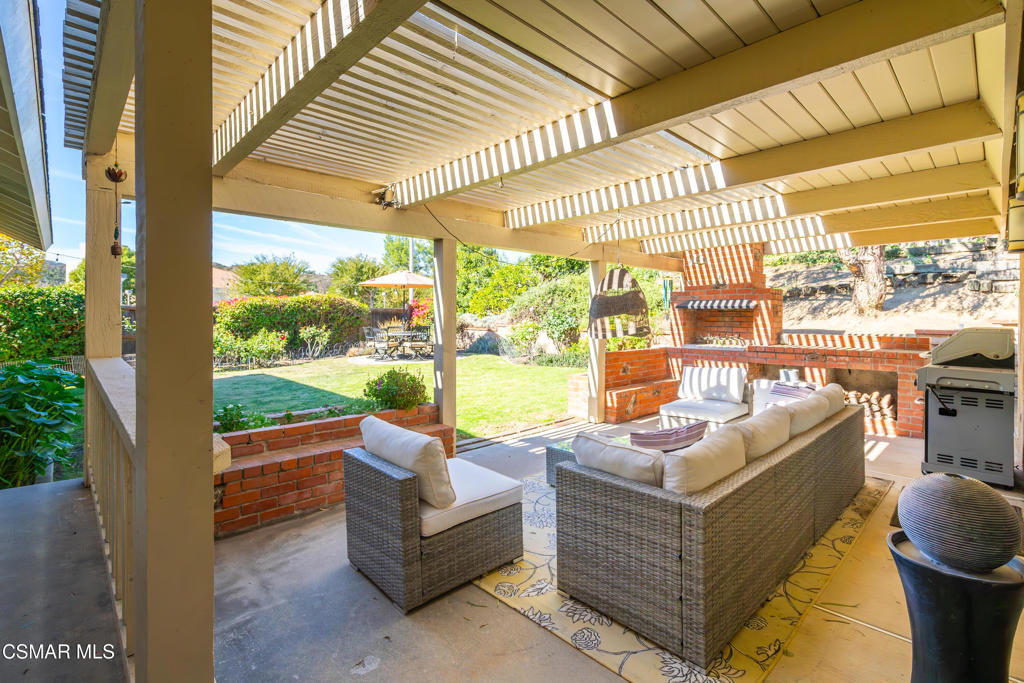 Covered patio with pergola, wicker seating, brick fireplace, and a view of the backyard.