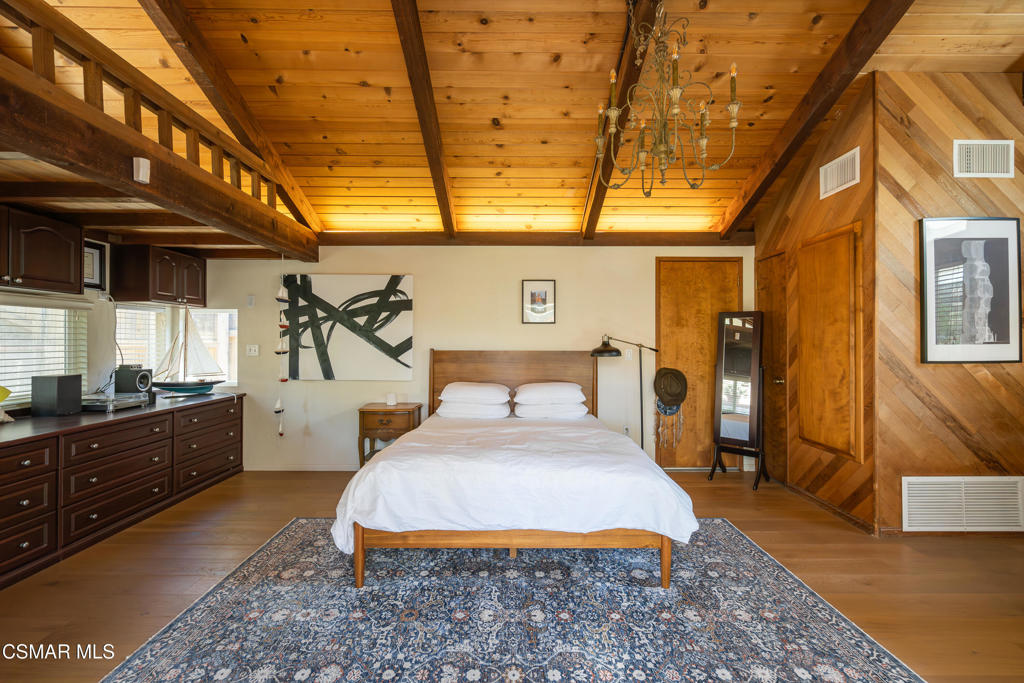 Bedroom with a vaulted wood ceiling, white bedding, dark cabinetry, and a blue patterned rug.