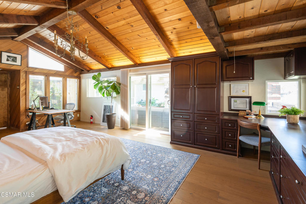Bedroom with vaulted wood-plank ceiling, bed, built-in cabinetry, and desk.
