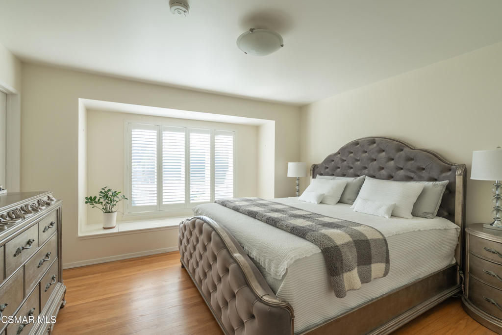 Bedroom with a tufted gray bed, white bedding, checkered throw, and shuttered windows.