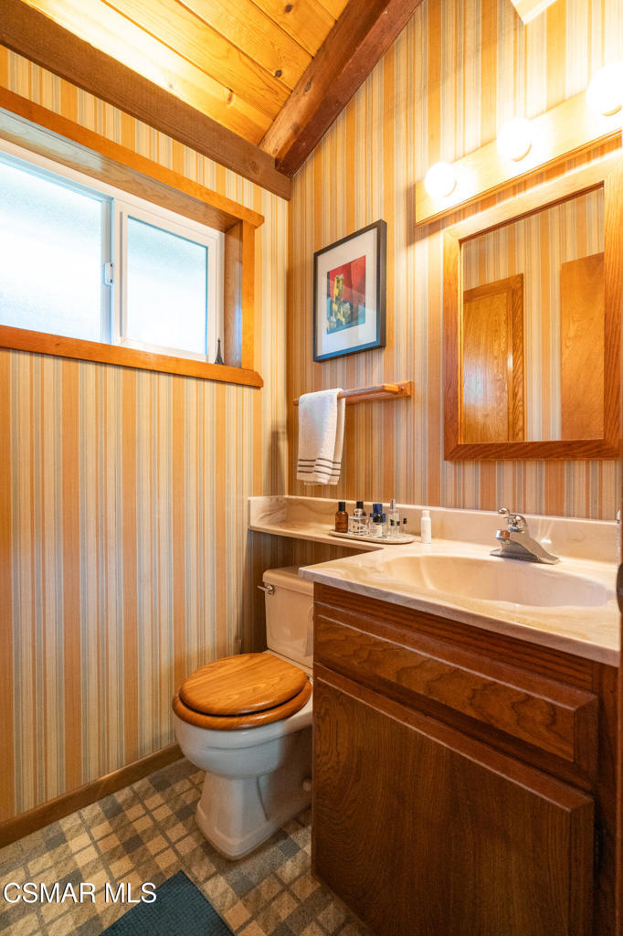 Bathroom with striped walls, exposed wood ceiling beams, and a wooden vanity.
