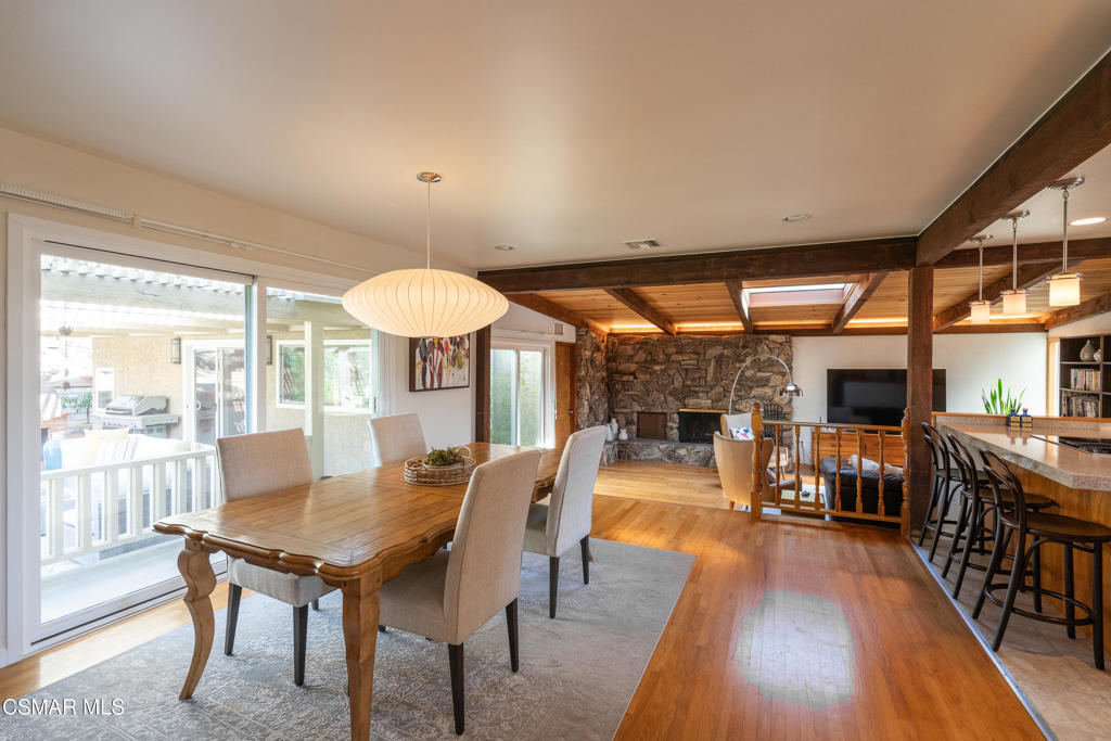 Dining area with a wooden table, exposed ceiling beams, and an adjoining stone fireplace.
