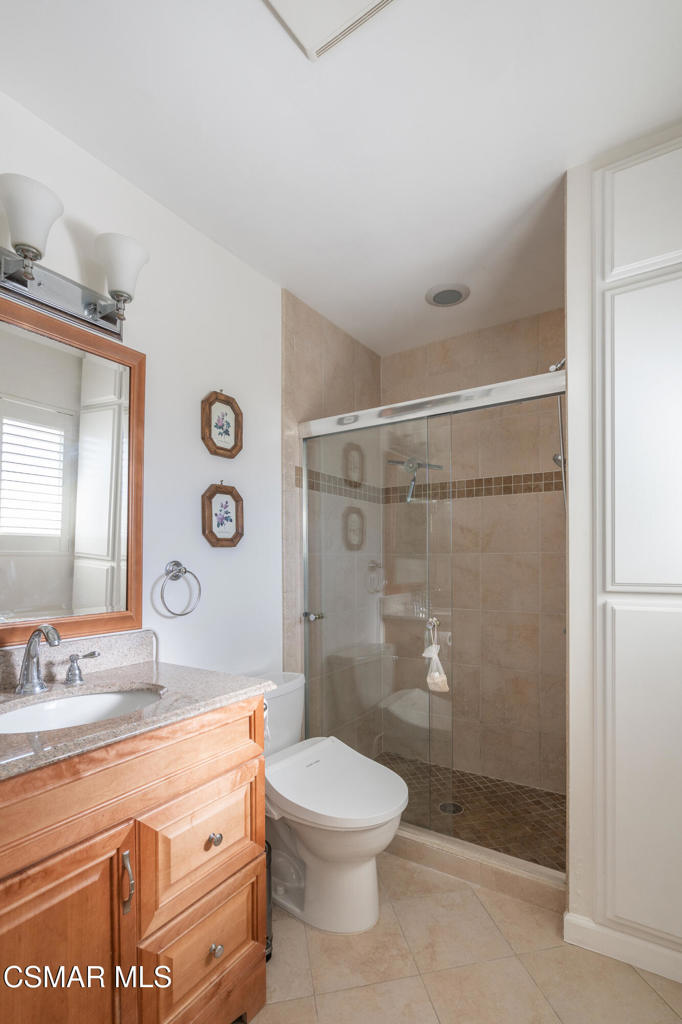 Bathroom with a wood vanity and granite counter beside a glass-enclosed tiled shower.