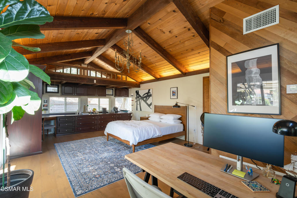 Bedroom with a vaulted wood-plank ceiling, exposed beams, and an integrated desk workspace.