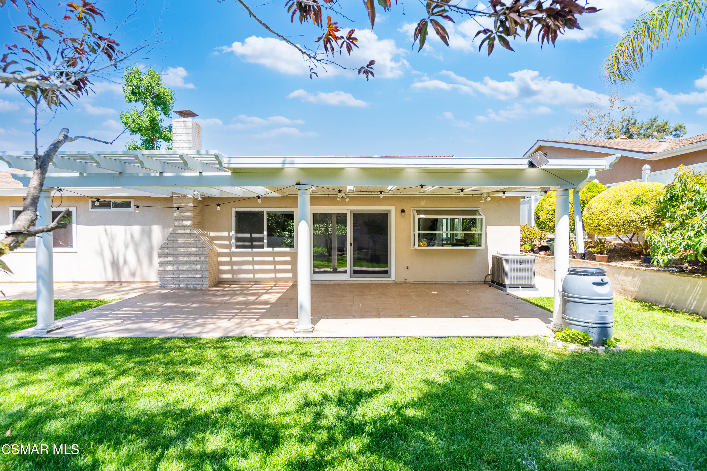 Home’s backyard patio with a white pergola, brick fireplace, and broad green lawn.