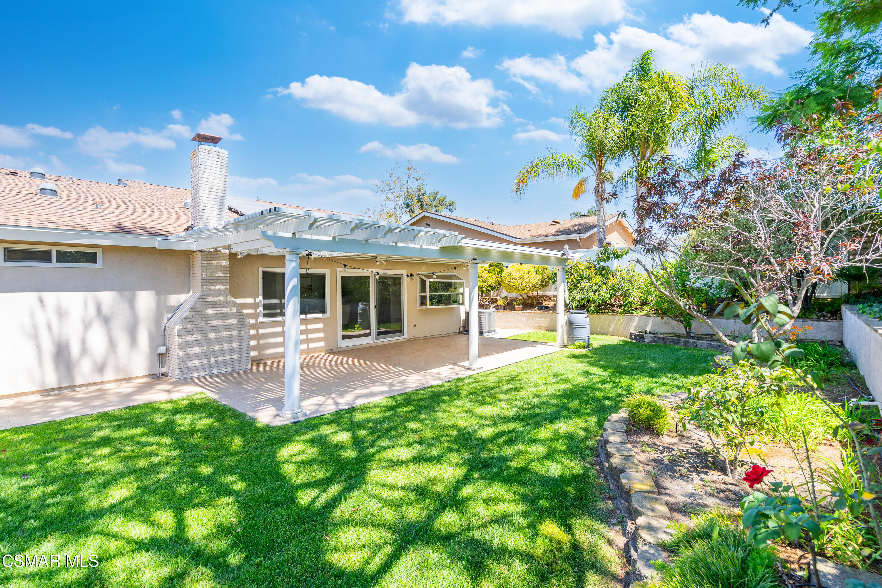 Backyard with a covered patio, brick fireplace, green lawn, and landscaped garden.