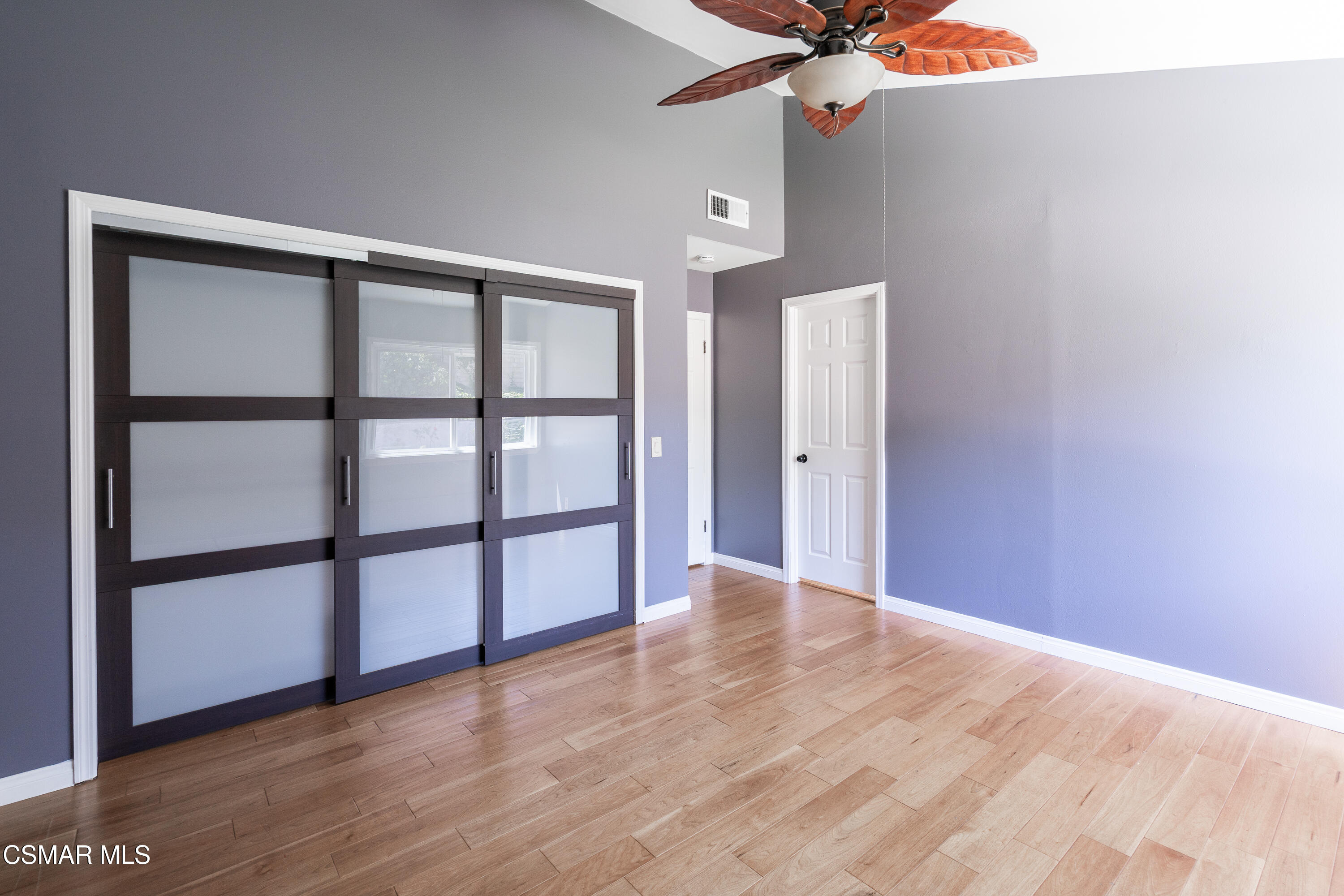 Empty bedroom with dark-framed frosted-glass closet doors and light wood flooring.