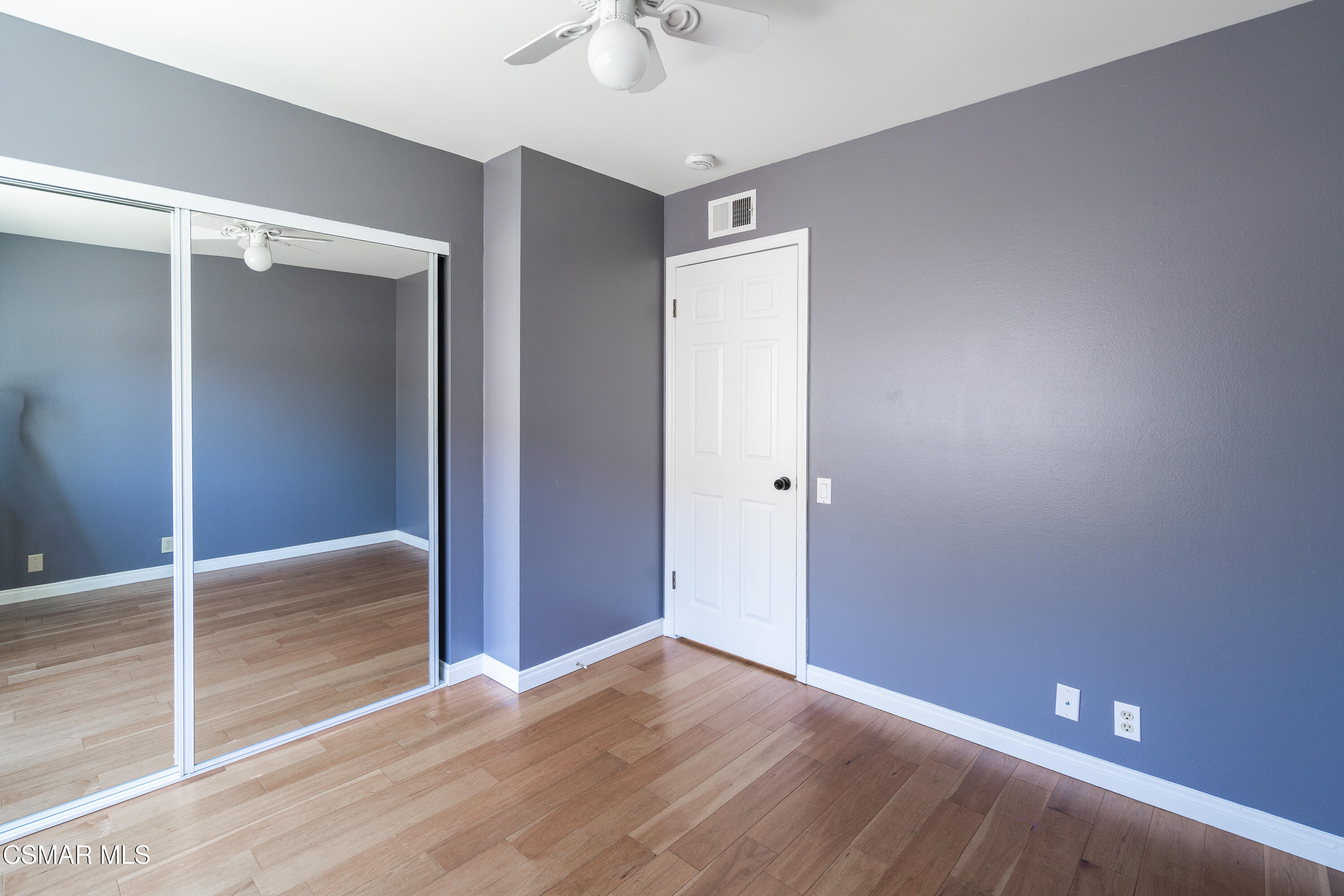 Empty bedroom with wood flooring and mirrored sliding closet doors.