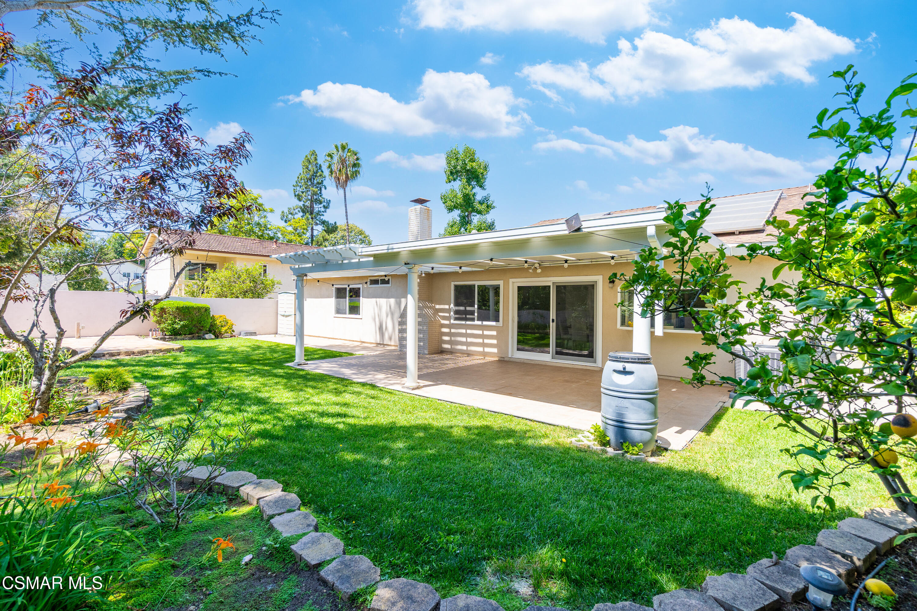 Backyard with a covered patio, green lawn, garden beds, rooftop solar panels, and a rain barrel.