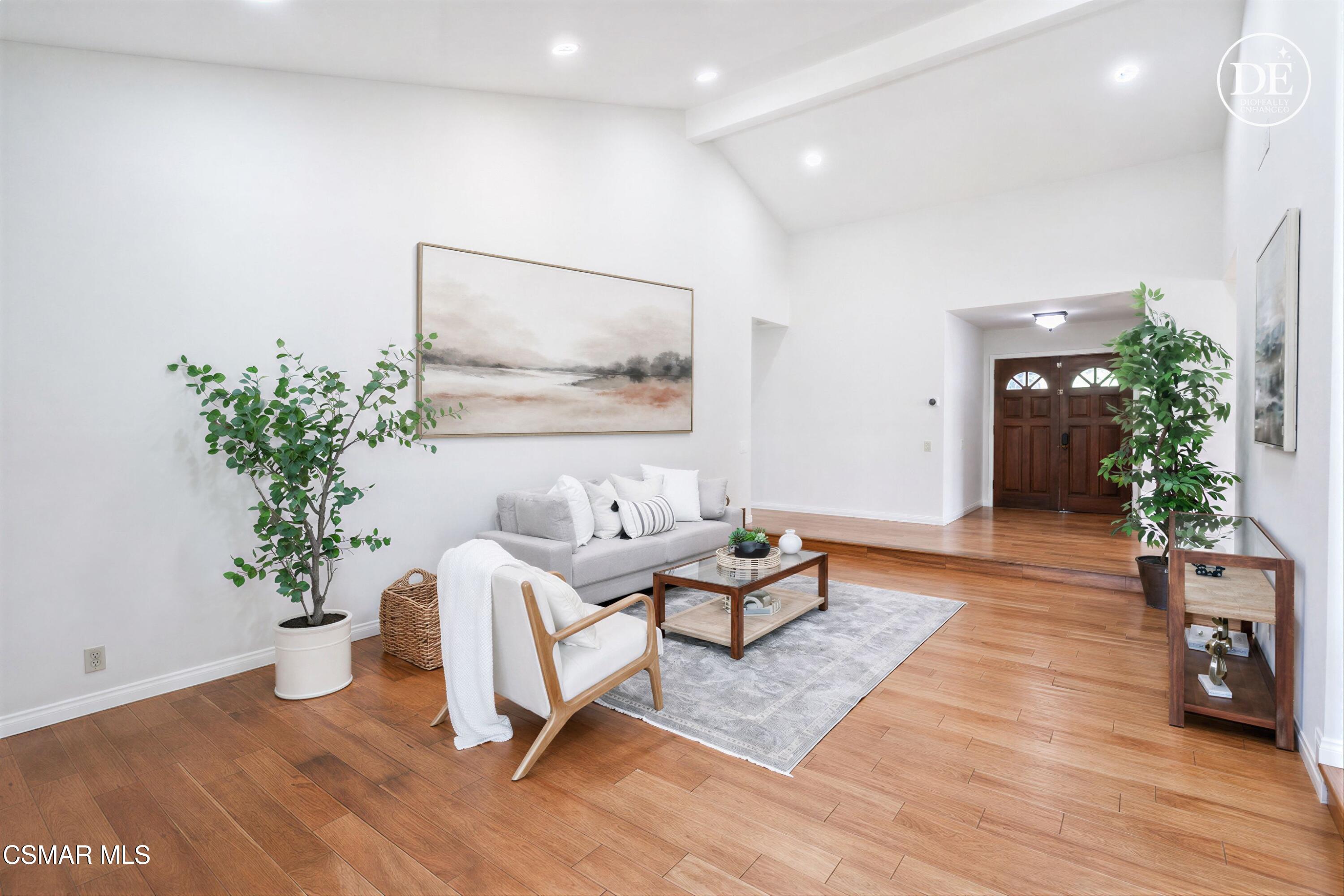 Staged living room with vaulted ceiling, gray sofa, warm wood floors, and dark wood double entry doors.