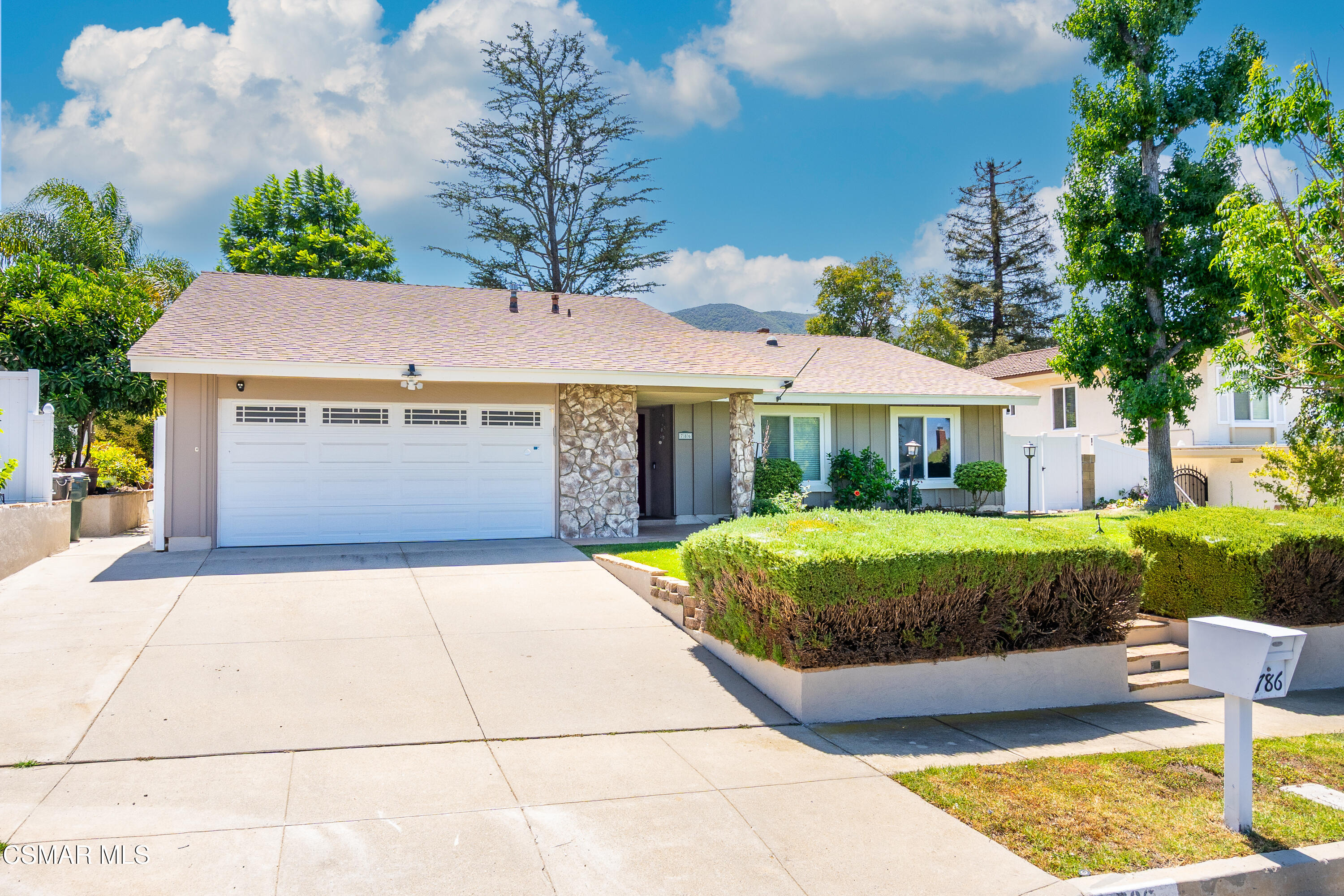 Single-story home with a two-car garage, stone accents, and a neatly trimmed hedge along the driveway.