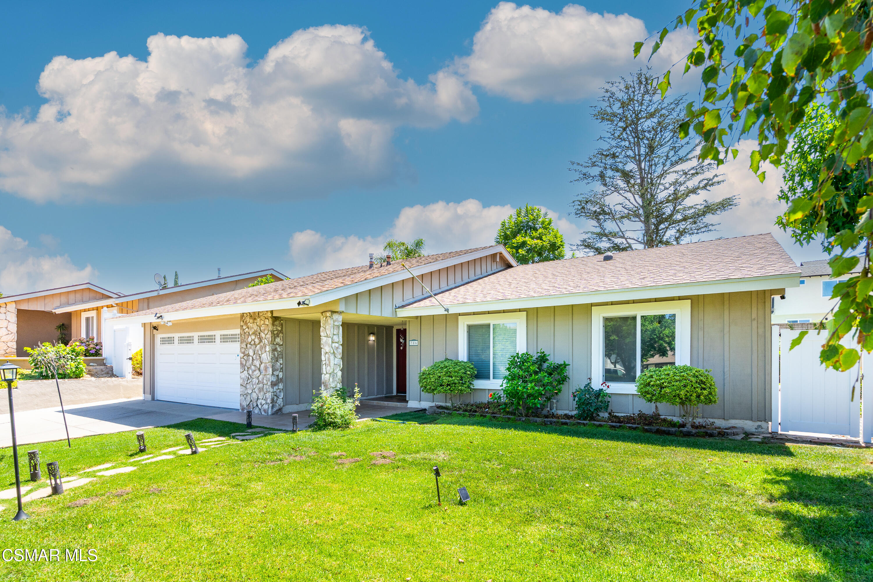 Single-story gray home with a white garage, stone porch columns, and a broad green front lawn.