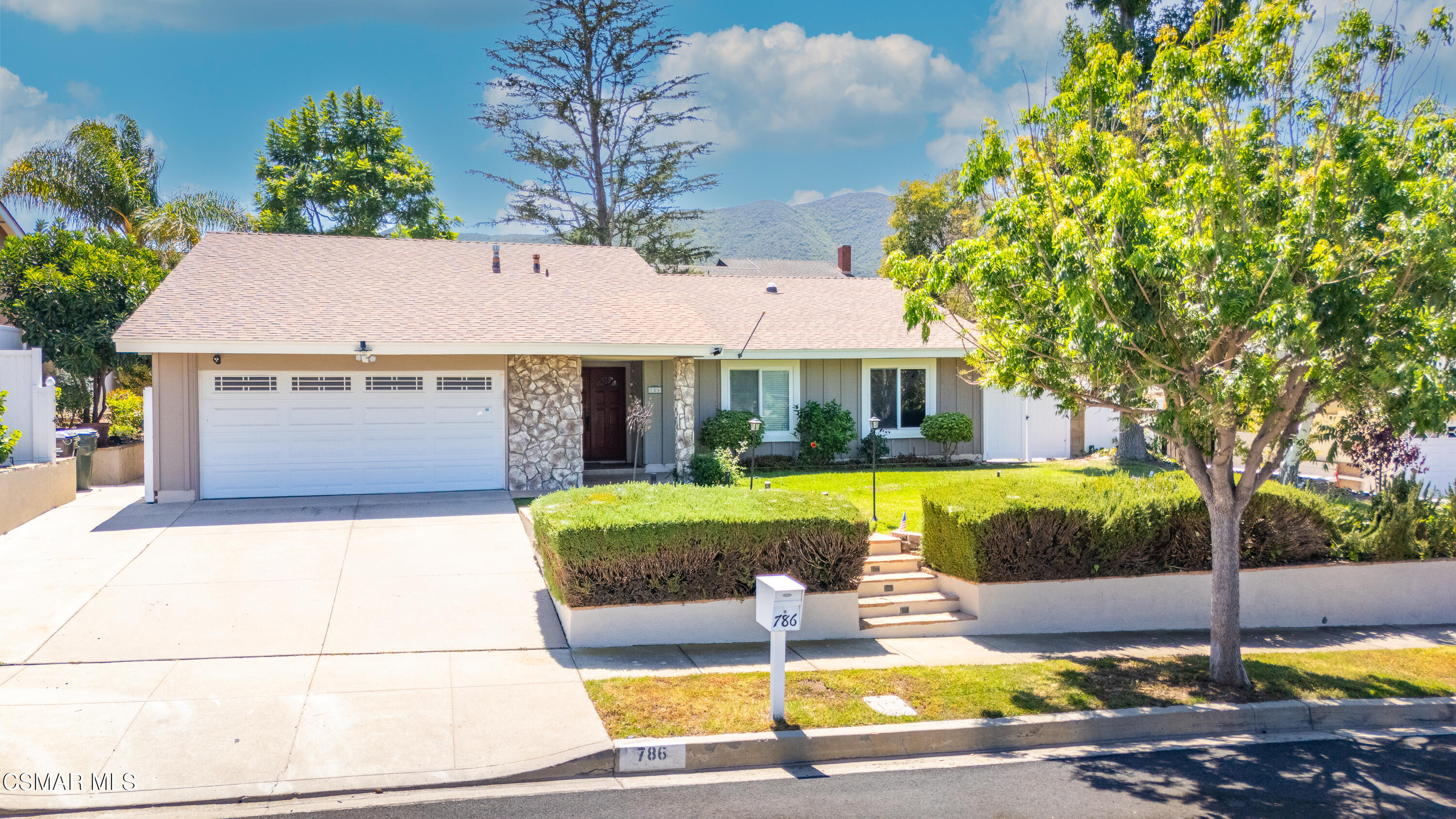 Single-story home with stone accents, a two-car garage, landscaped yard, and mountains behind it.