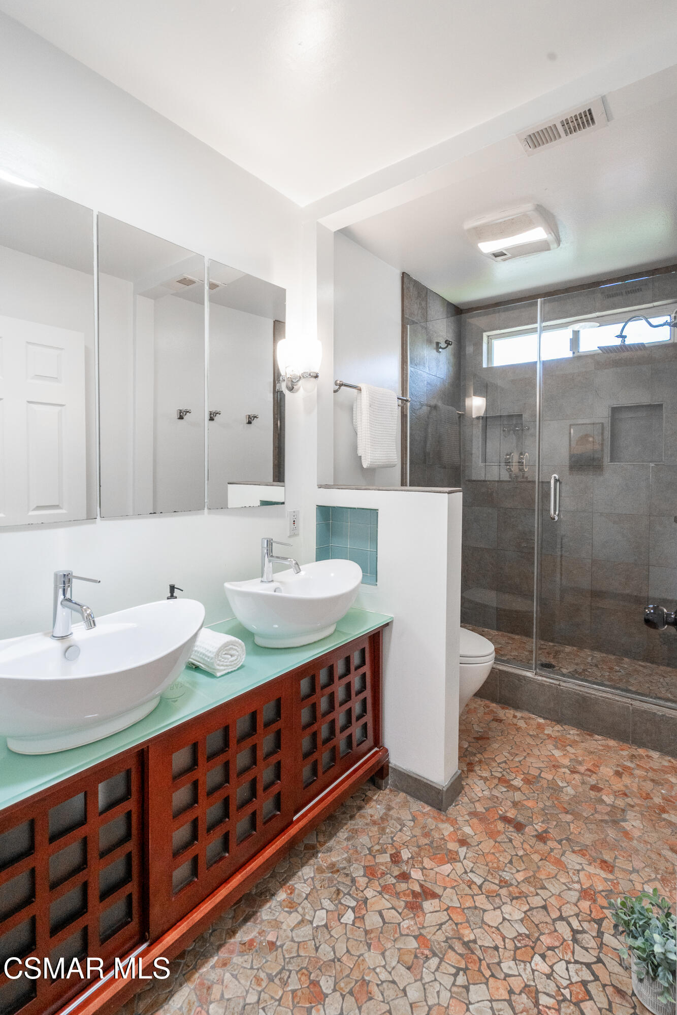 Bathroom with double vessel sinks, a wood vanity, and a glass-enclosed tiled shower.