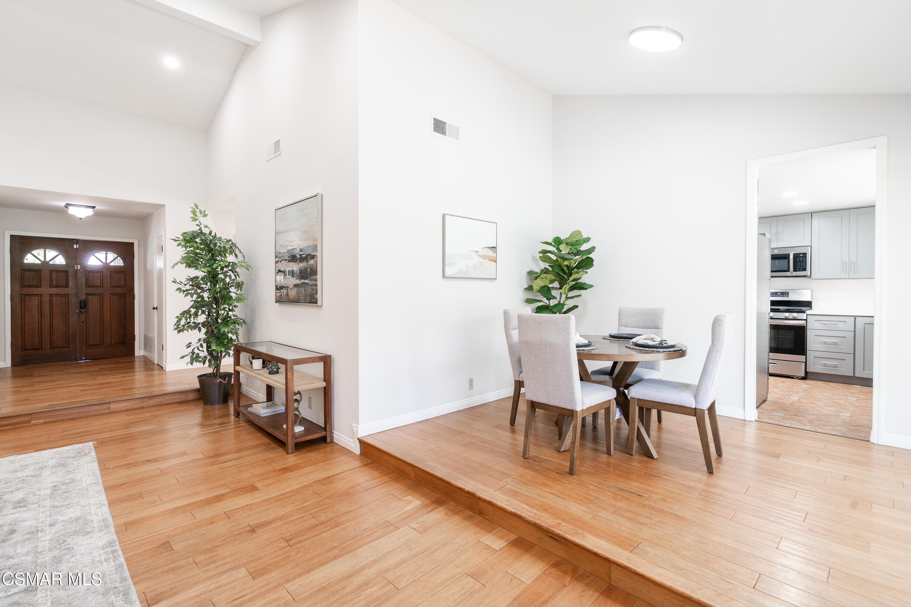 Dining area on a raised hardwood platform beside the double front door, with the kitchen visible through a doorway.