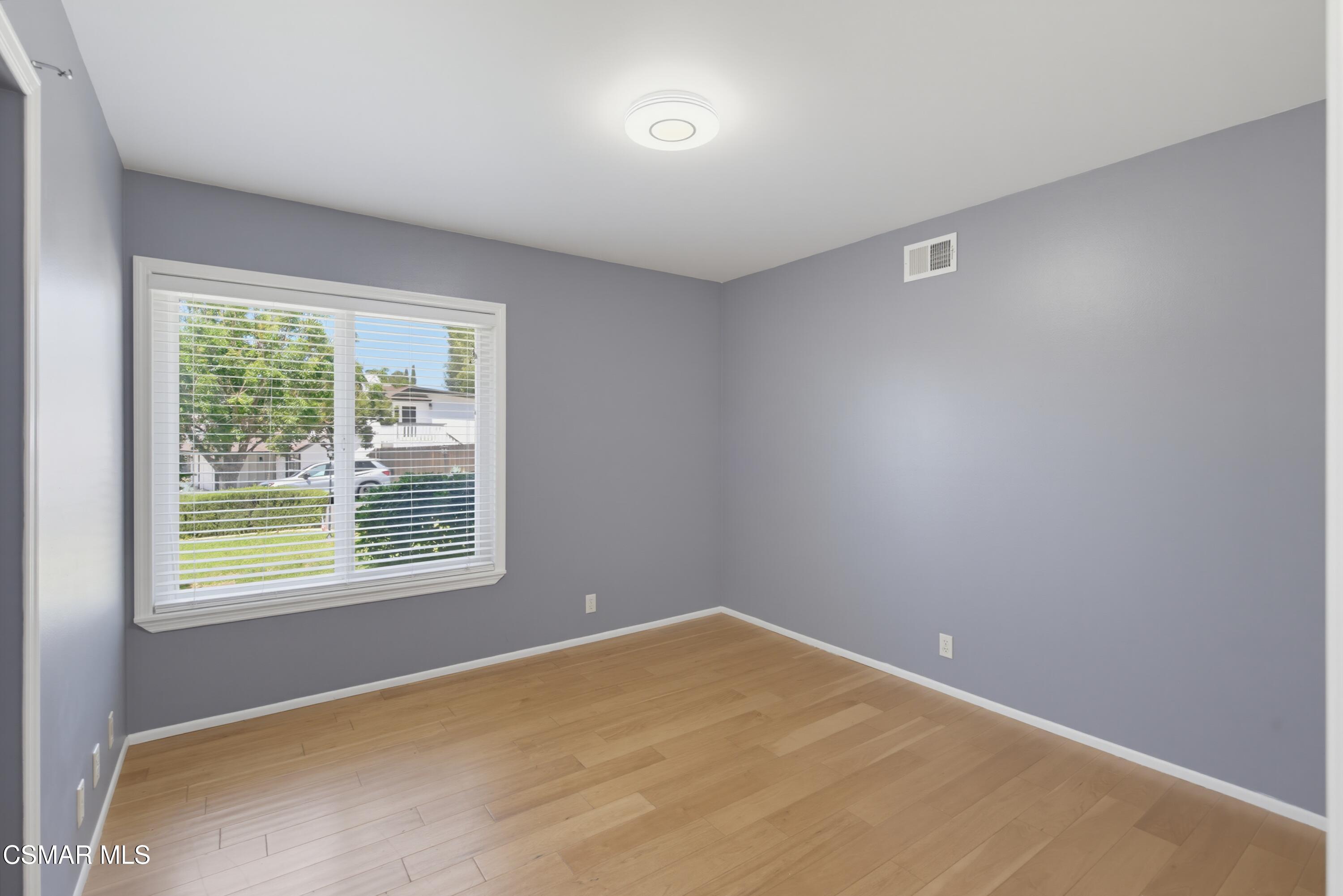 Empty bedroom with gray walls, light wood flooring, and a large window with white blinds.