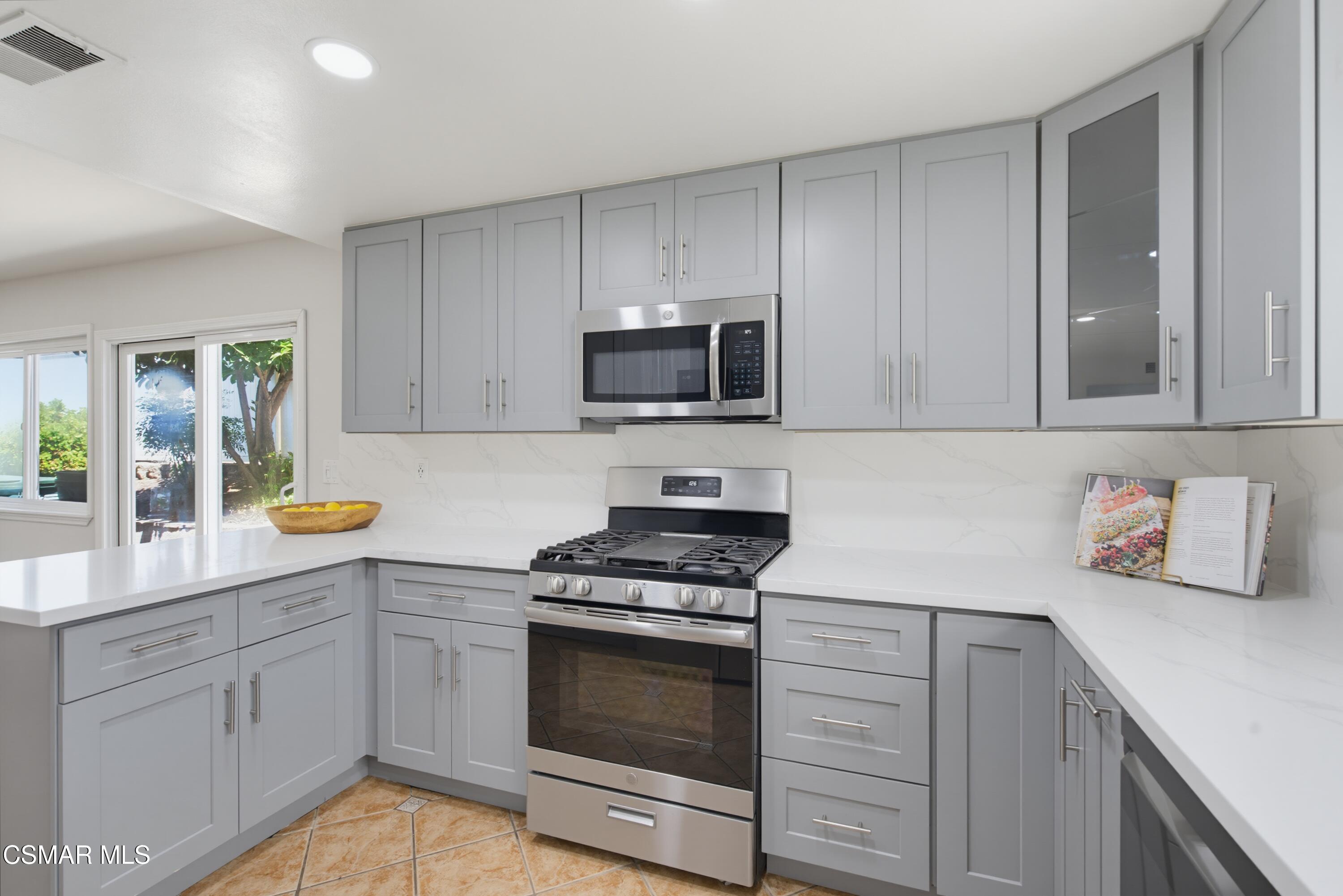 Kitchen with gray cabinets, white counters, stainless steel appliances, and a sliding glass door to the yard.