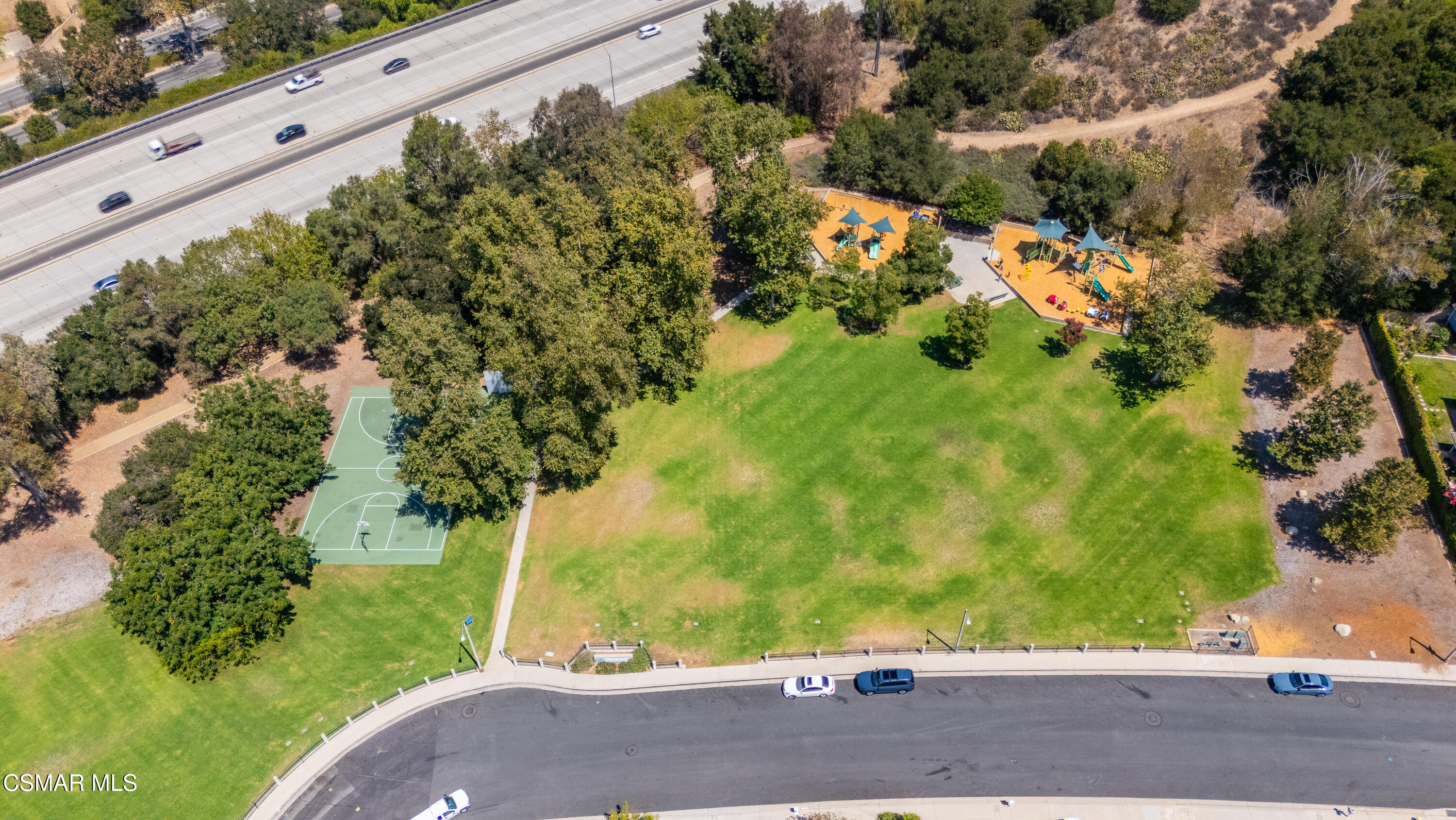 Aerial view of a grassy park with a basketball court and two playgrounds.