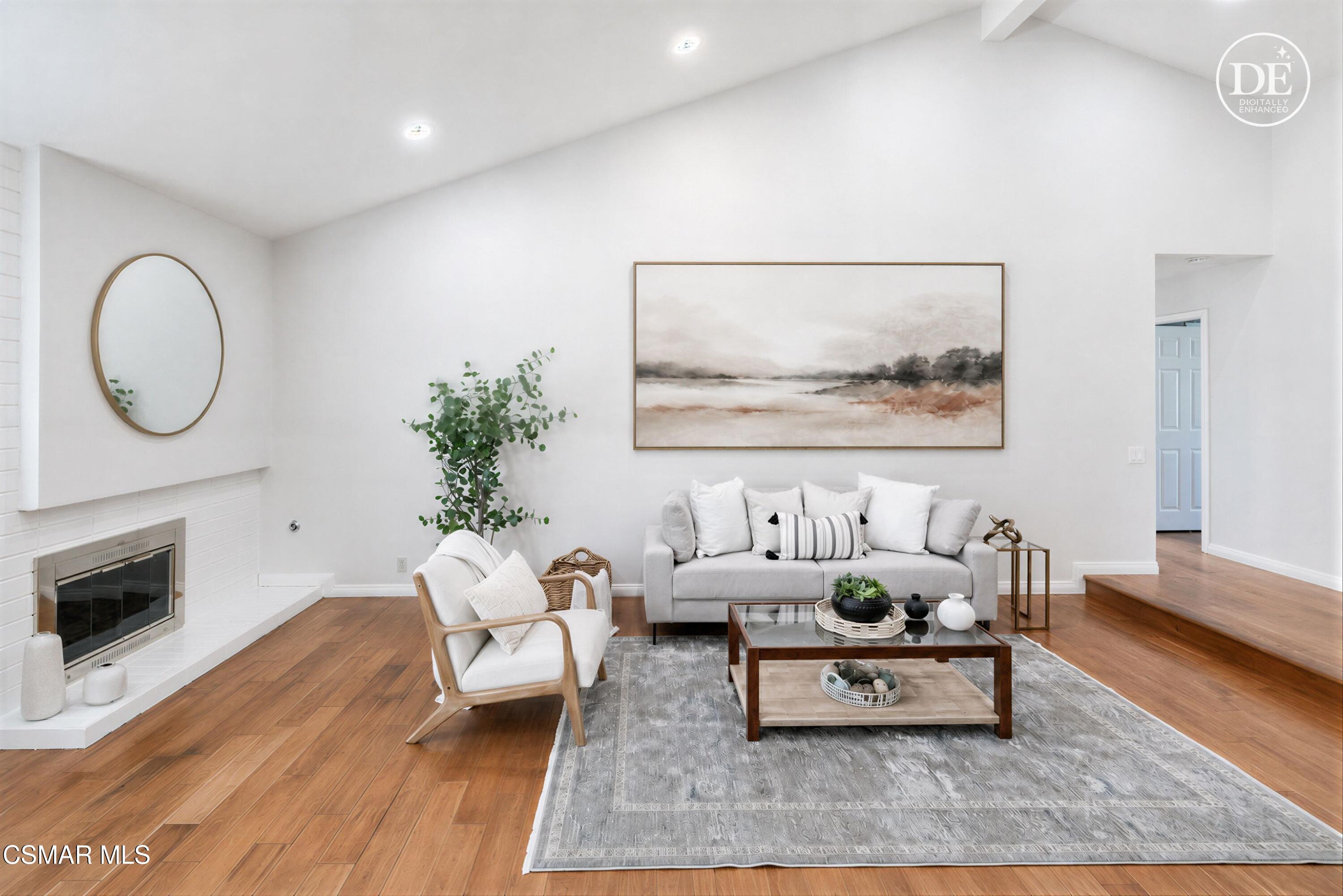 Staged living room with a white fireplace, gray sofa, and warm-toned hardwood floors.