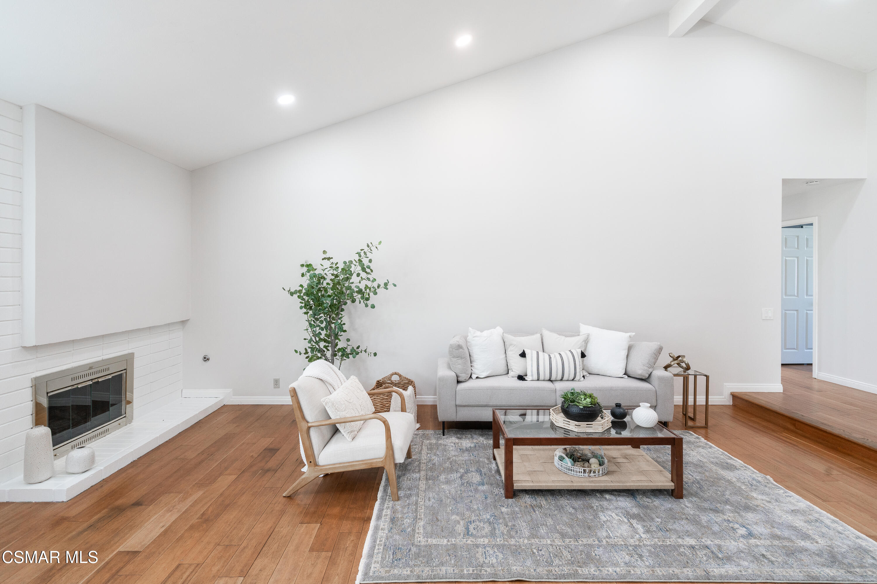 Staged living room with a white tiled fireplace, gray sofa, and hardwood floors.