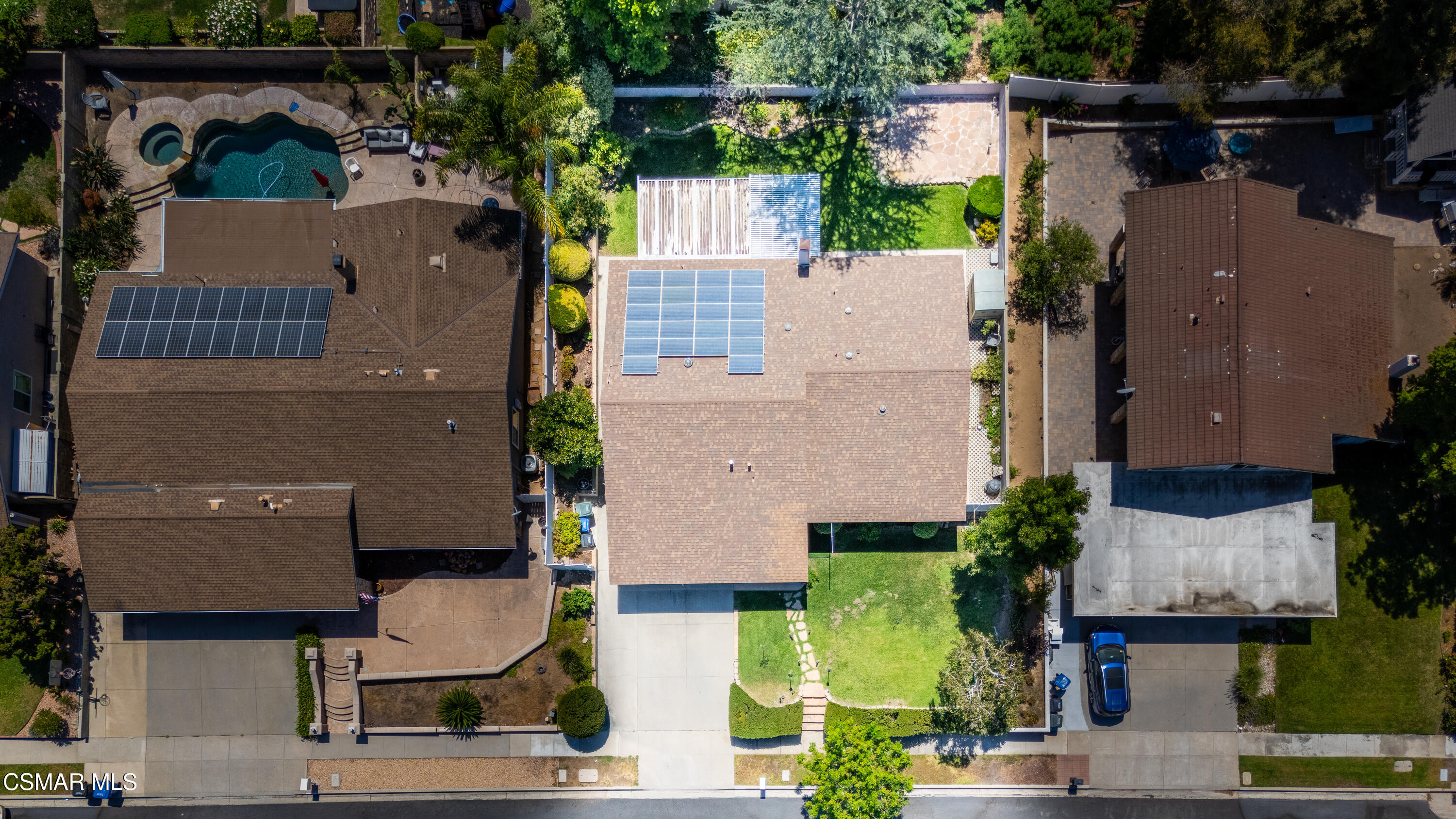 Aerial view of a home with rooftop solar panels, a front lawn, and a backyard pool and spa.