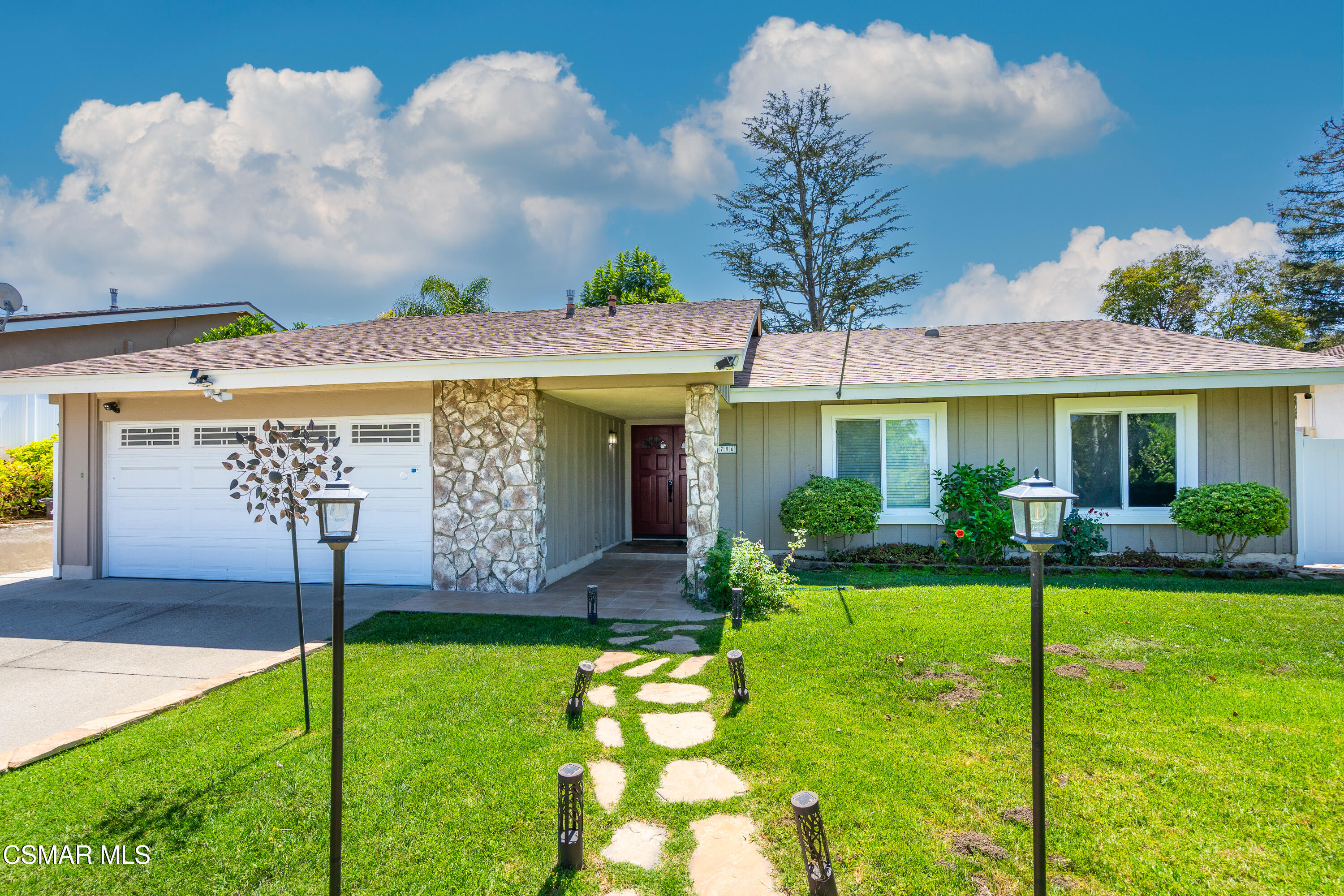 Single-story home with stone entry columns, double garage, and a green lawn with stepping-stone path.