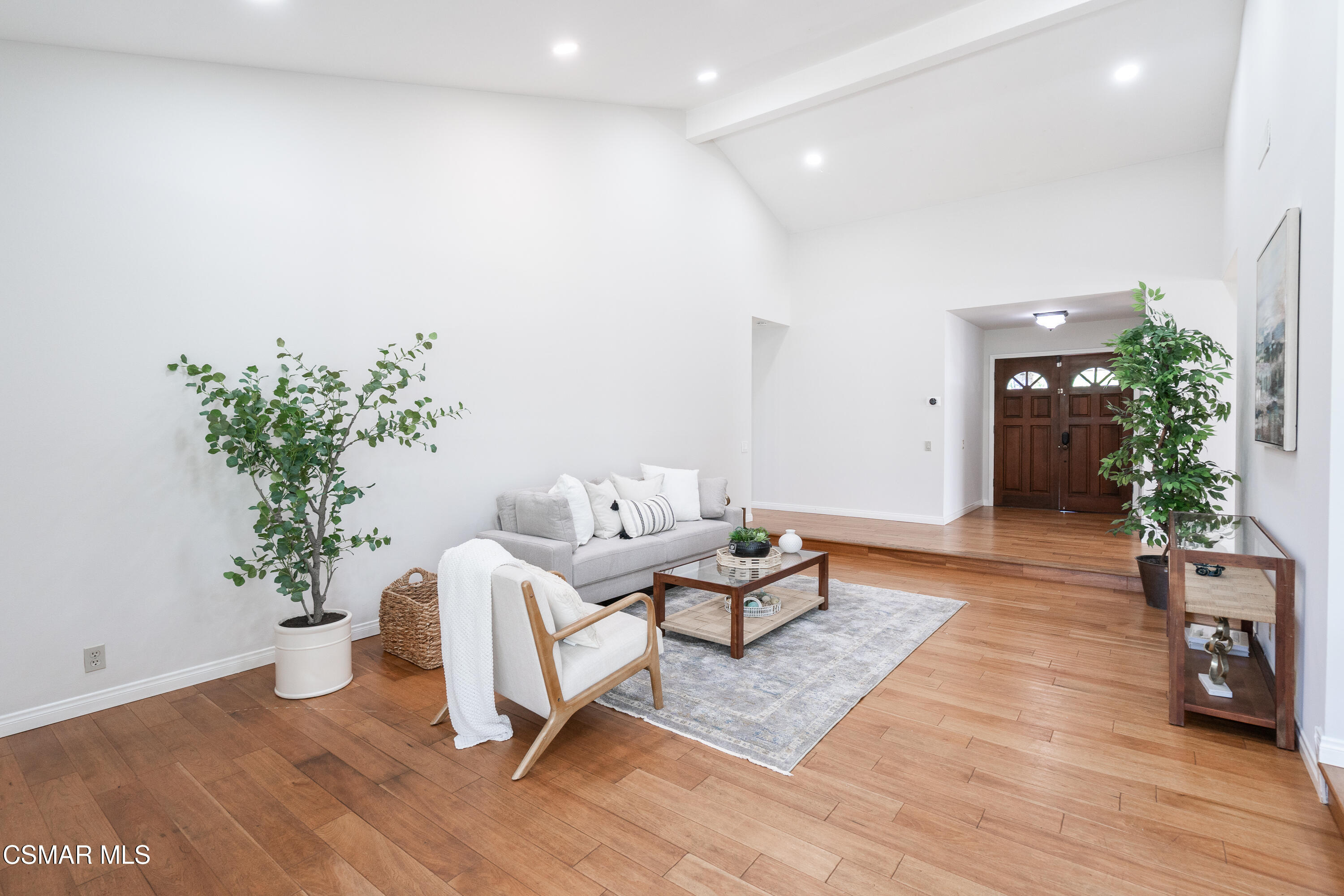 Staged living room with hardwood floors, a gray sofa, white armchair, and dark wood double front doors.