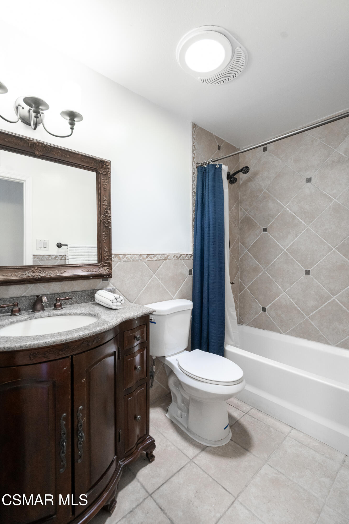 Bathroom with a carved dark wood vanity, ornate mirror, and tiled tub-shower behind a blue curtain.