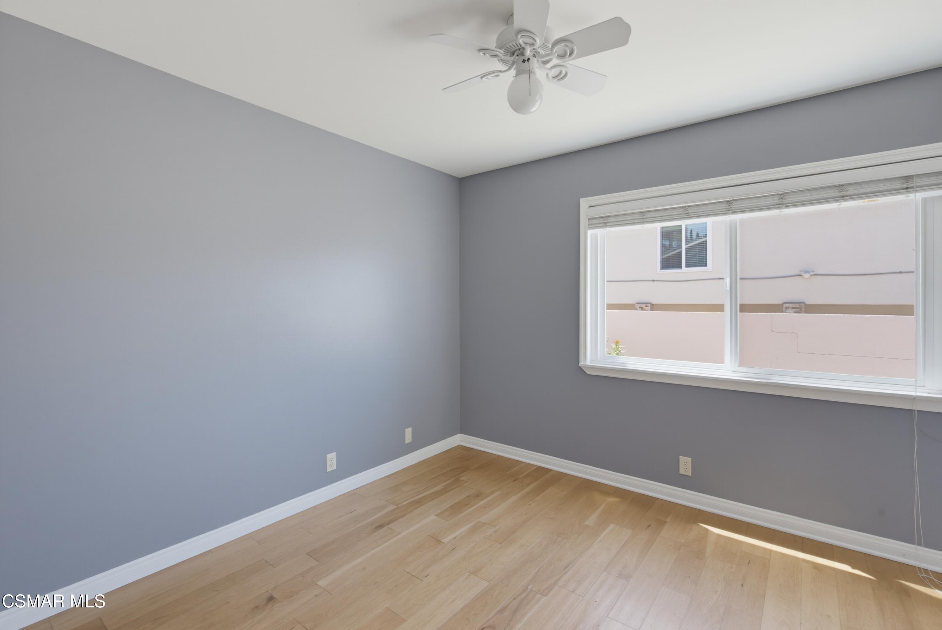 Empty bedroom with gray walls, light wood flooring, and a wide window with blinds.