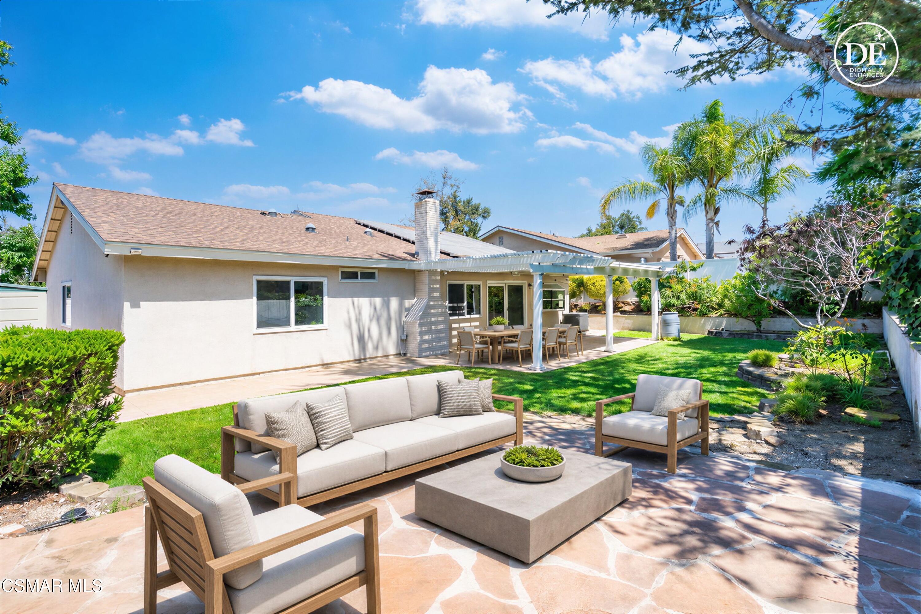 Backyard patio with covered dining area, stone terrace lounge seating, green lawn, and palm trees.