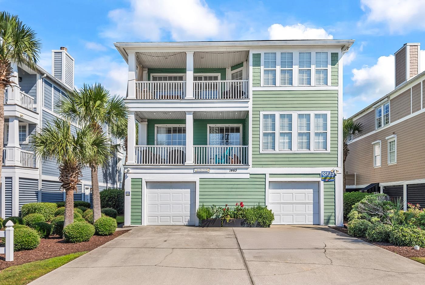 Green coastal-style home at 1463 Basin Trail with two balconies, white trim, and palm trees.